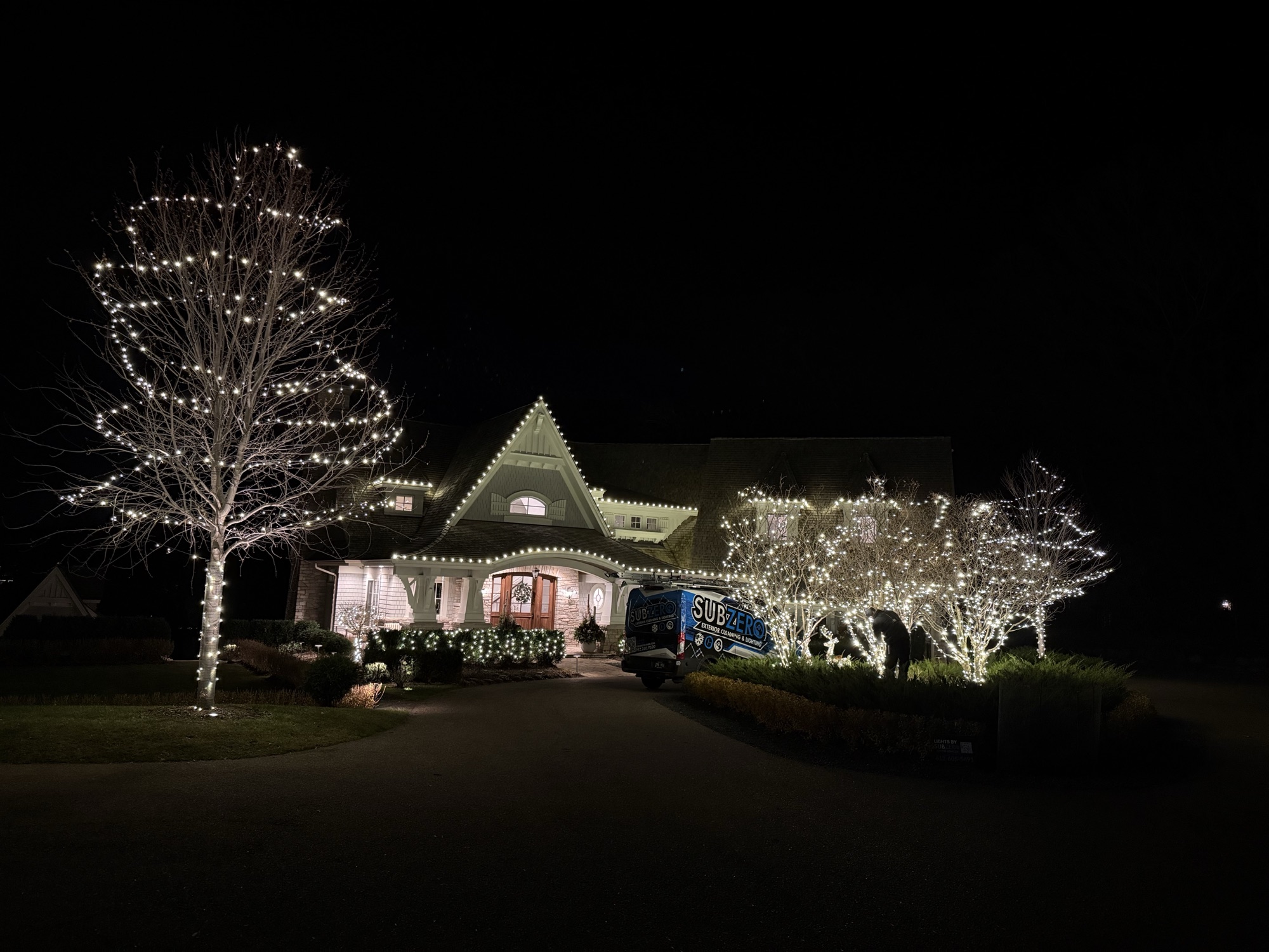 Warm white Christmas lights on a home and trees by Sub Zero