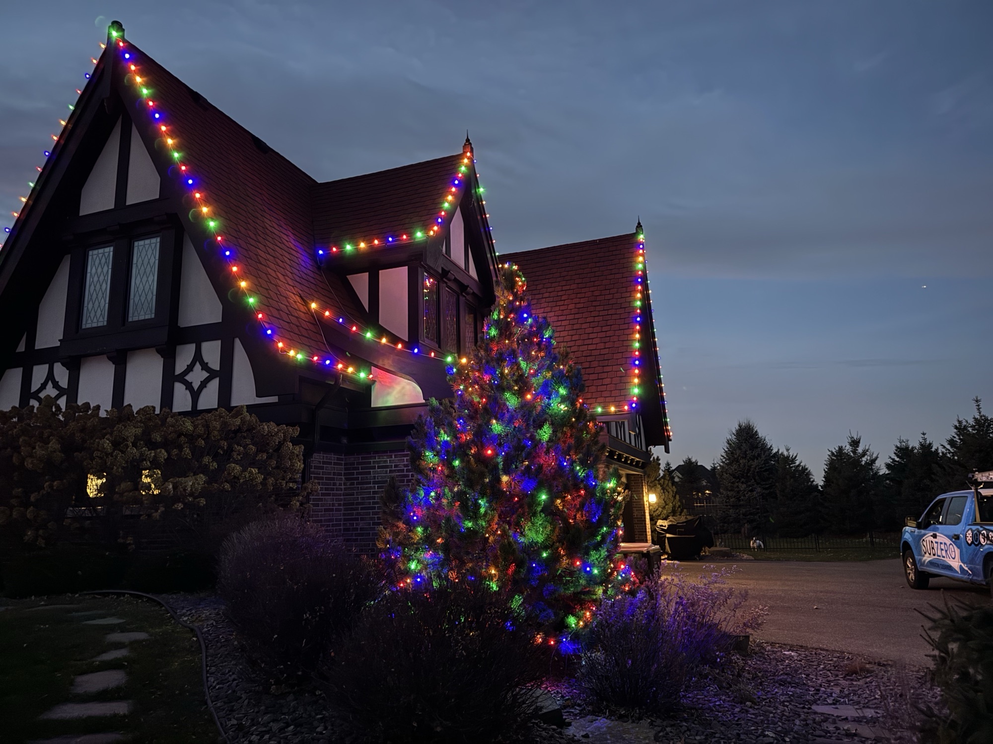 Multicolor roofline Christmas lights and lit evergreen tree